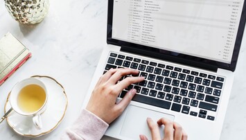 Typend persoon aan bureau met laptop en thee